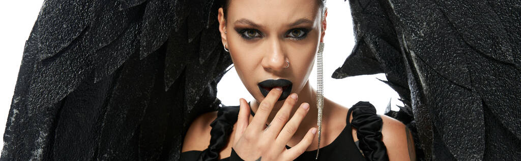 retrato de mujer seductora en maquillaje oscuro y traje de demonio negro tocando labios en blanco, bandera - Foto, Imagen