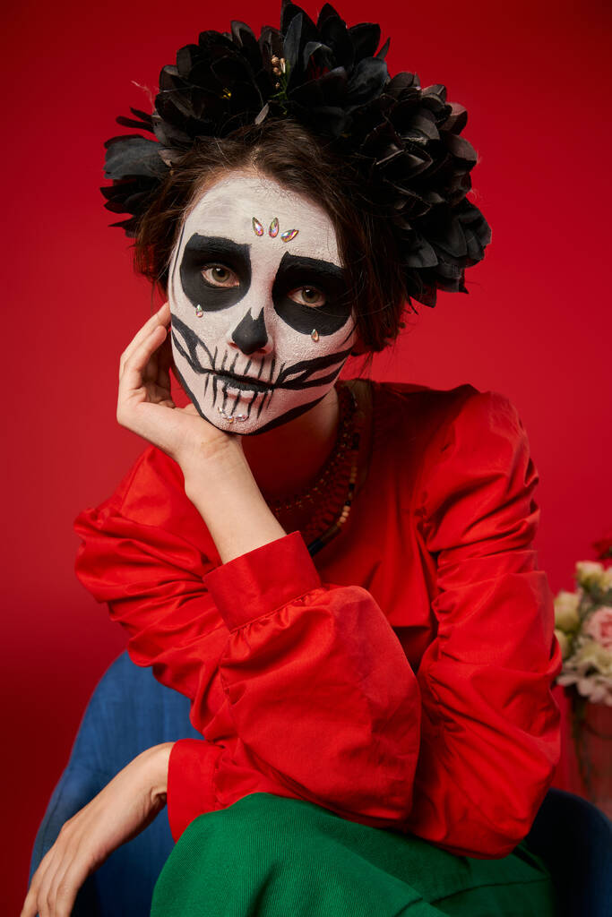 πορτρέτο της γυναίκας στο μακιγιάζ κρανίο και μαύρο στεφάνι κοιτάζοντας κάμερα στο κόκκινο, Ημέρα των Νεκρών παράδοση - Φωτογραφία, εικόνα