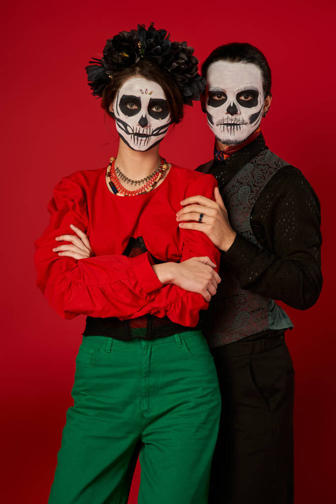 dia de los muertos paar in griezelige make-up, man omarmen vrouw met gevouwen armen op rood, banner - Foto, afbeelding