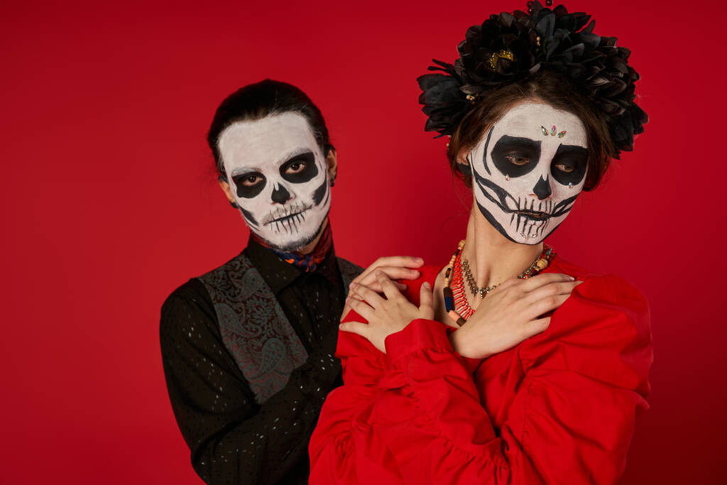 mulher em maquiagem crânio e coroa preta posando com braços cruzados perto de homem assustador no vermelho, Dia dos Mortos - Foto, Imagem