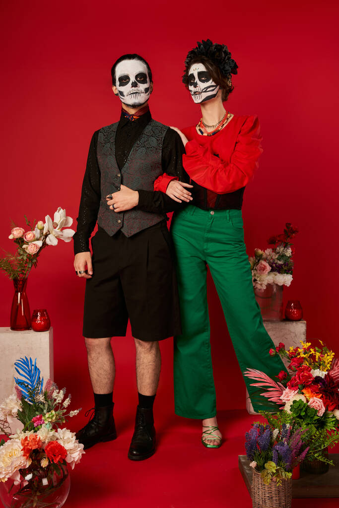 повна довжина пари в макіяжі черепа біля традиційного Дня Мертвих Ренди з квітами на червоному - Фото, зображення
