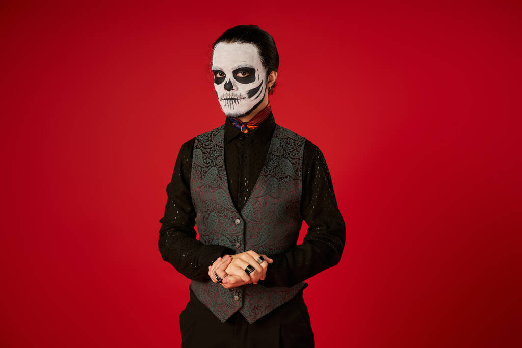elegante hombre en espeluznante día de los muertos cráneo maquillaje mirando a la cámara en rojo, la tradición mexicana - Foto, imagen