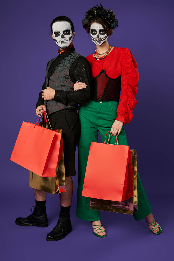 μοντέρνα dia de los muertos ζευγάρι στο κρανίο μακιγιάζ στέκεται με τσάντες για ψώνια σε μπλε, εποχιακή πώληση - Φωτογραφία, εικόνα