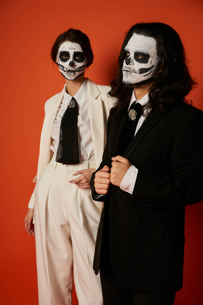 woman in catrina makeup and white suit looking at camera near scary man on red, dia de lost muertos - Photo, Image
