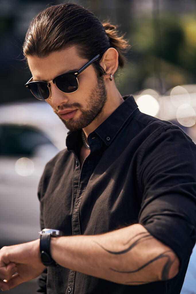 vertikale Aufnahme eines gut aussehenden männlichen Modells im eleganten schwarzen Outfit mit Blick auf seine Armbanduhr, Mode - Foto, Bild