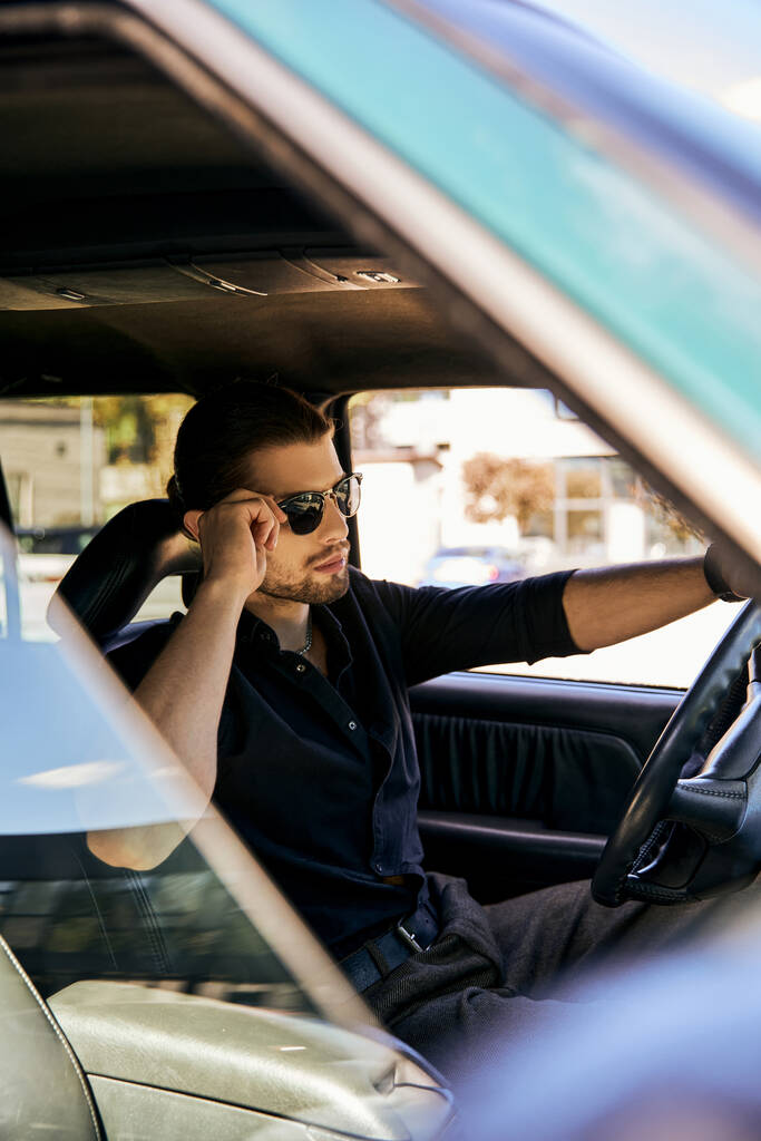 İyi görünümlü bir adam, direksiyon başında dinleniyor ve güneş gözlüklerine dokunuyor, seksi sürücü. - Fotoğraf, Görsel