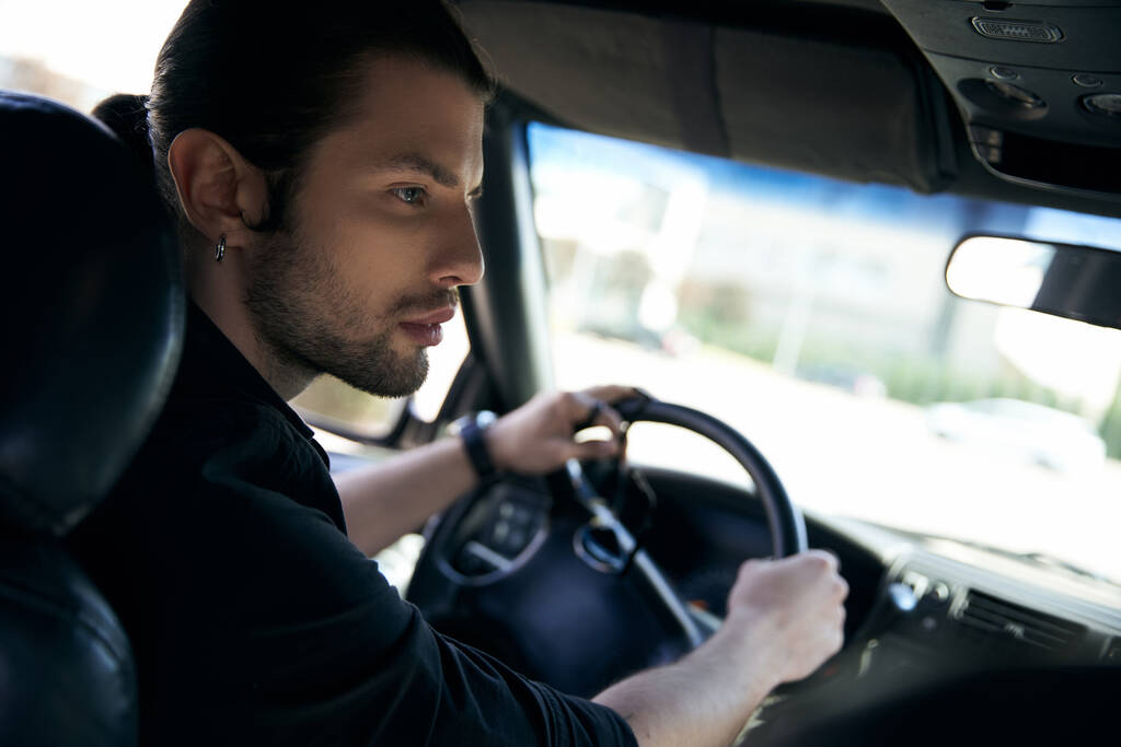 sexy hombre elegante con pendiente y reloj de pulsera en traje negro que conduce su coche, concepto de moda - Foto, Imagen