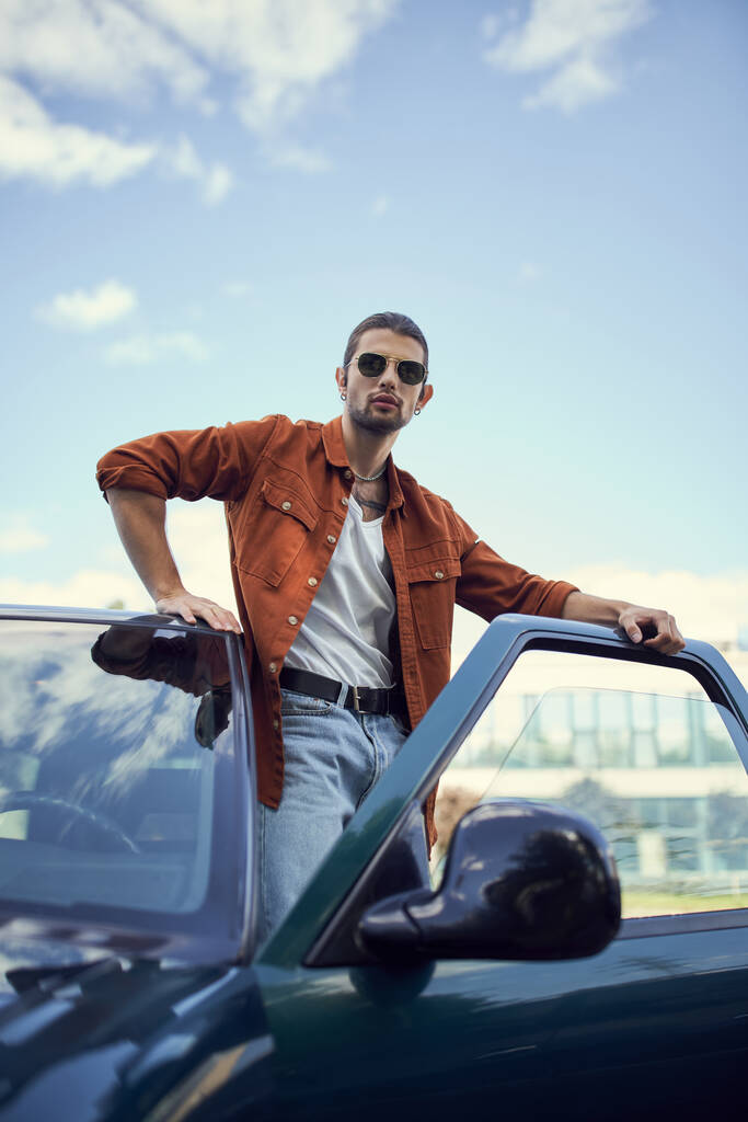 függőleges lövés vonzó fiatalember elegáns élénk ruhát pózol mellett autója, divat - Fotó, kép