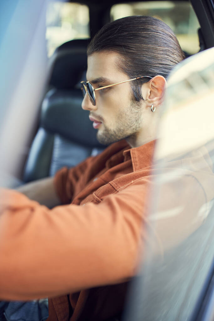 vertikální záběr stylového okouzlujícího muže s culíkem a příslušenstvím na volantu, sexy řidič - Fotografie, Obrázek