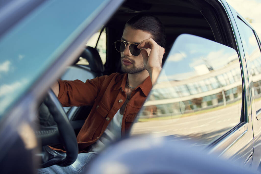 tempting young male model with elegant accessories and ponytail behind steering wheel, fashion - Photo, Image