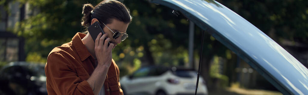 jovem bonito com olhar dapper e óculos de sol falando com sua seguradora por telefone, banner - Foto, Imagem