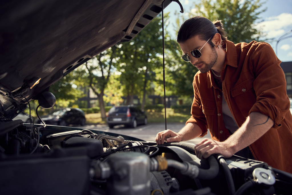 thoughtful young sexy driver with sunglasses and beard looking attentively at his car engine - Photo, Image