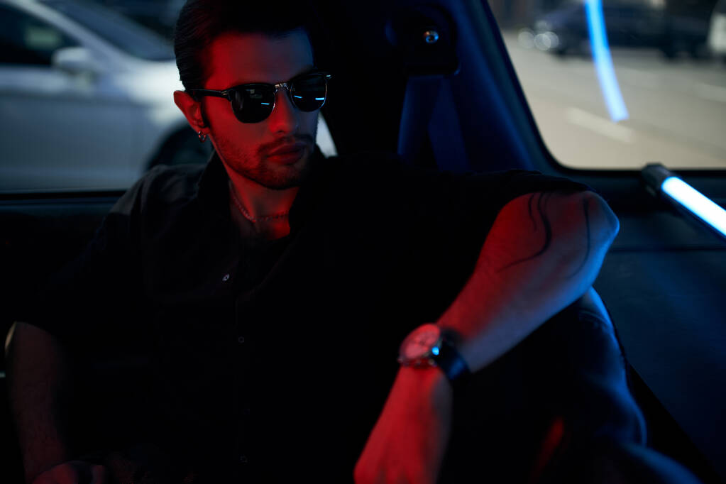 bello sexy driver in camicia nera con occhiali da sole e tatuaggio in posa nella sua auto, concetto di moda - Foto, immagini