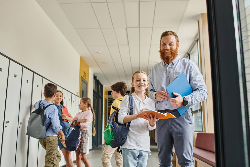 A male teacher passionately engages with a group of kids in a lively hallway, sharing knowledge and sparking curiosity. - Photo, Image