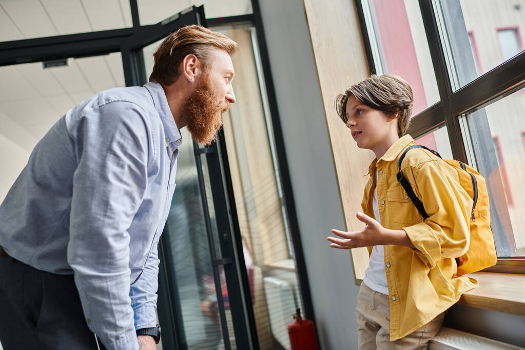 Ein Mann steht neben einem kleinen Jungen vor einem Fenster und führt ein nachdenkliches Gespräch, während er nach draußen schaut.. - Foto, Bild
