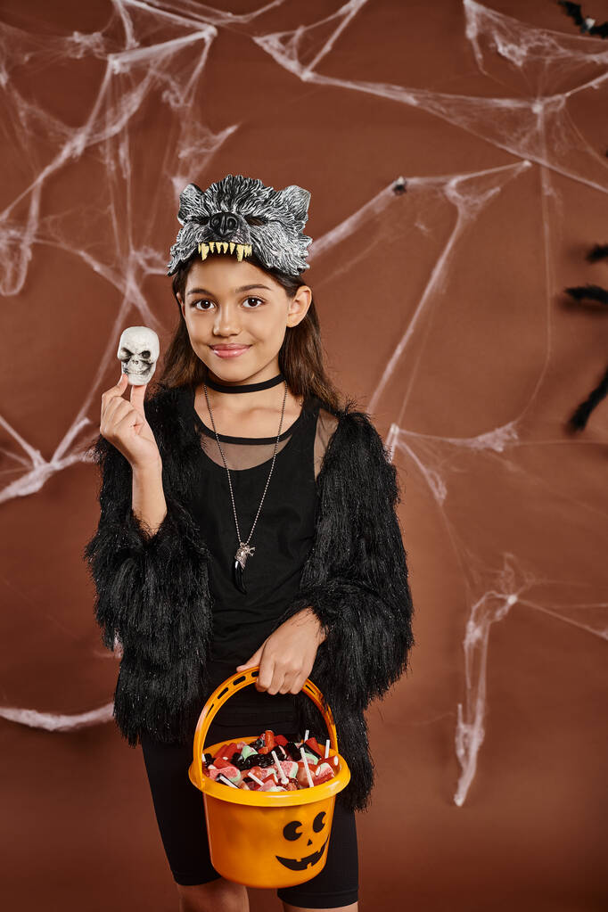 close up smiley preteen girl with bucket of sweets holding a Halloween skull, Halloween concept - Photo, Image