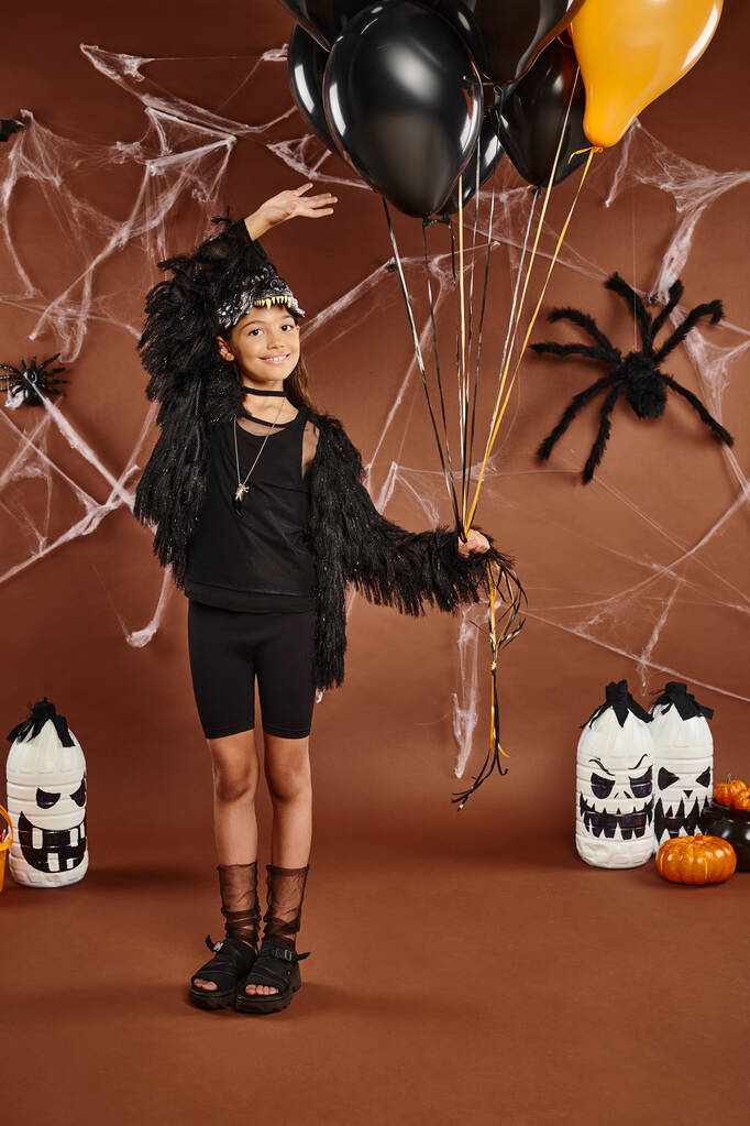 fröhliches Mädchen hält schwarze und orangefarbene Luftballons und berührt sie mit der Hand, Halloween-Konzept - Foto, Bild