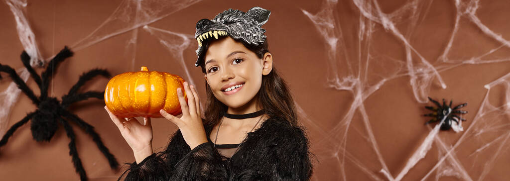 preteen girl holds pumpkin in her hands aside wearing wolf mask, Halloween concept, banner - Photo, Image