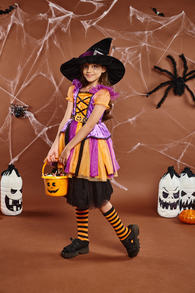 lindo preadolescente en sombrero de bruja sostiene cubo de dulces en el telón de fondo con linternas y arañas, Halloween - Foto, Imagen