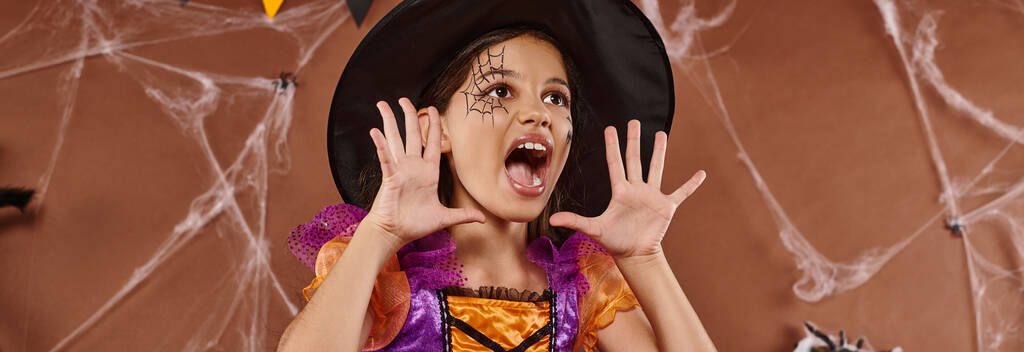 魔女の帽子と茶色の背景で叫ぶハロウィーンの衣装の感情的な少女,バナー - 写真・画像