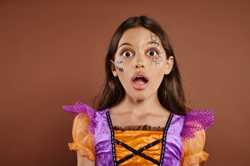 expresión de la cara, chica sorprendida en disfraz de Halloween mirando a la cámara en el fondo marrón, espeluznante - Foto, Imagen