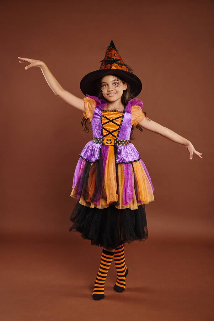 graziosa ragazza in costume di Halloween e cappello da strega in posa su sfondo marrone, concetto magico - Foto, immagini
