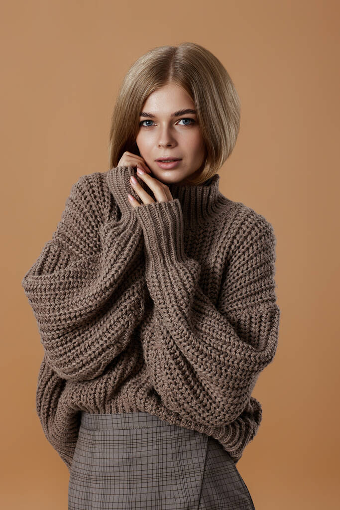 beautiful blonde woman in brown knitted sweater on beige background. autumn style - Photo, Image