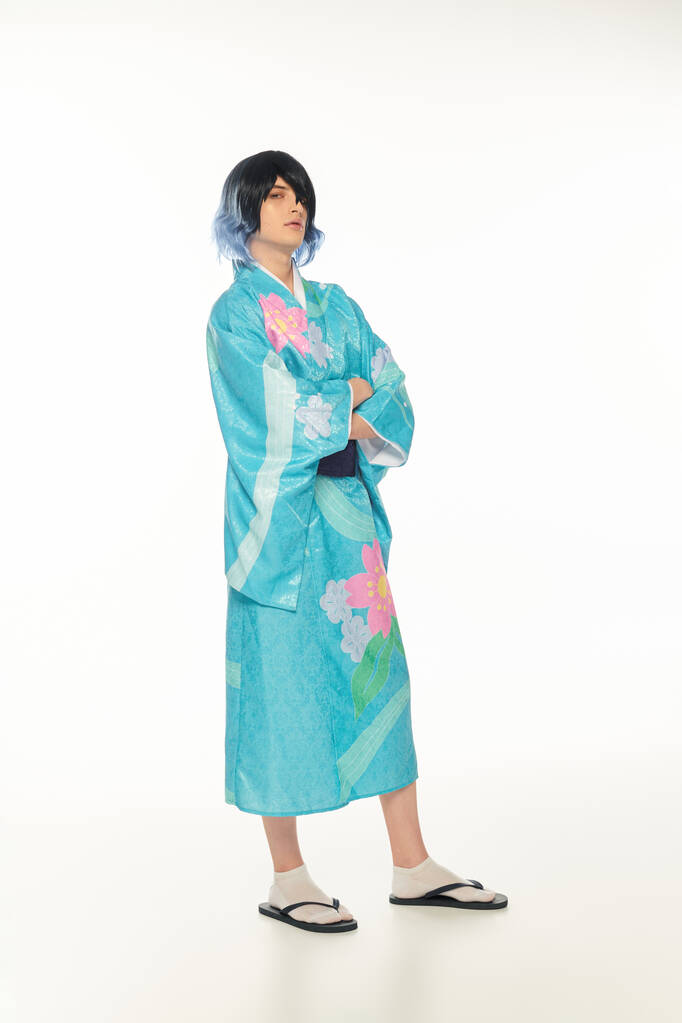 volledige lengte van de jonge man in kleurrijke kimono en pruik poseren met gekruiste armen op witte, cosplayer - Foto, afbeelding