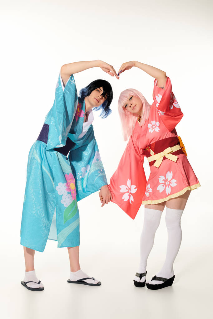 romantic cosplayers in wigs and bright kimonos showing great heart sign with hands on white - Photo, Image