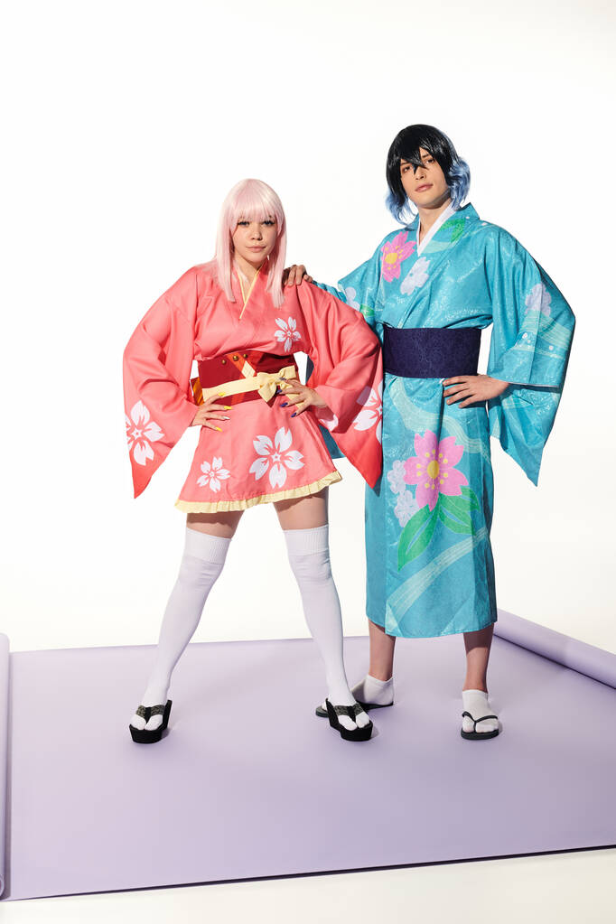 selbstbewusstes, ausdrucksstarkes Paar in farbenfrohen Kimonos und Flügeln, das mit den Händen an den Hüften posiert, Cosplay-Trend - Foto, Bild