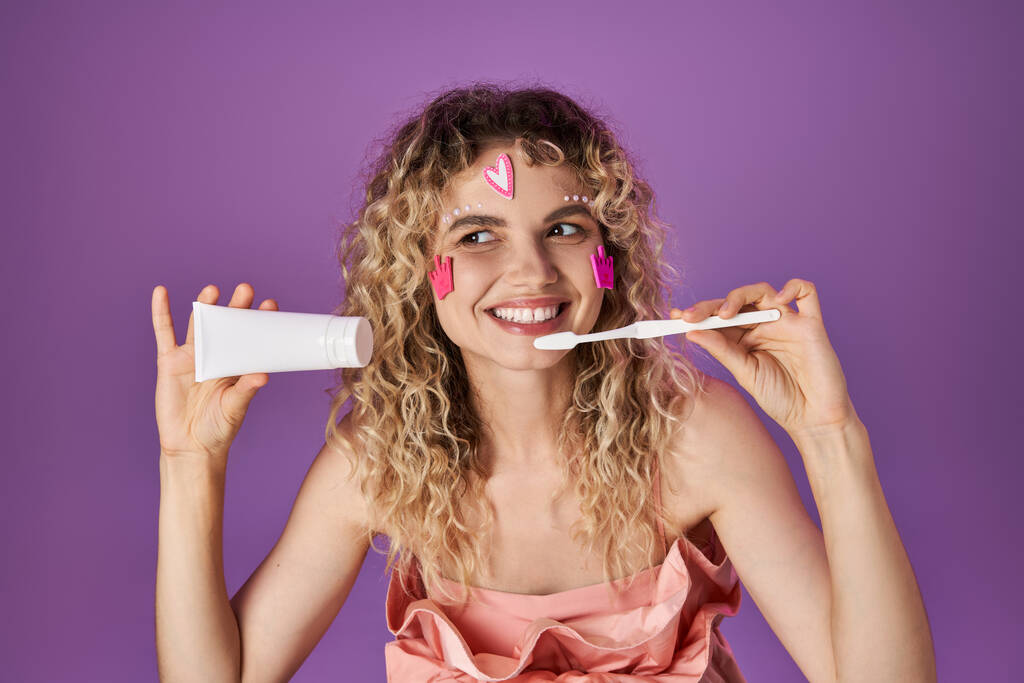 Fada de dente loira sorridente em traje rosa com adesivos faciais segurando escova de dentes e pasta dental - Foto, Imagem