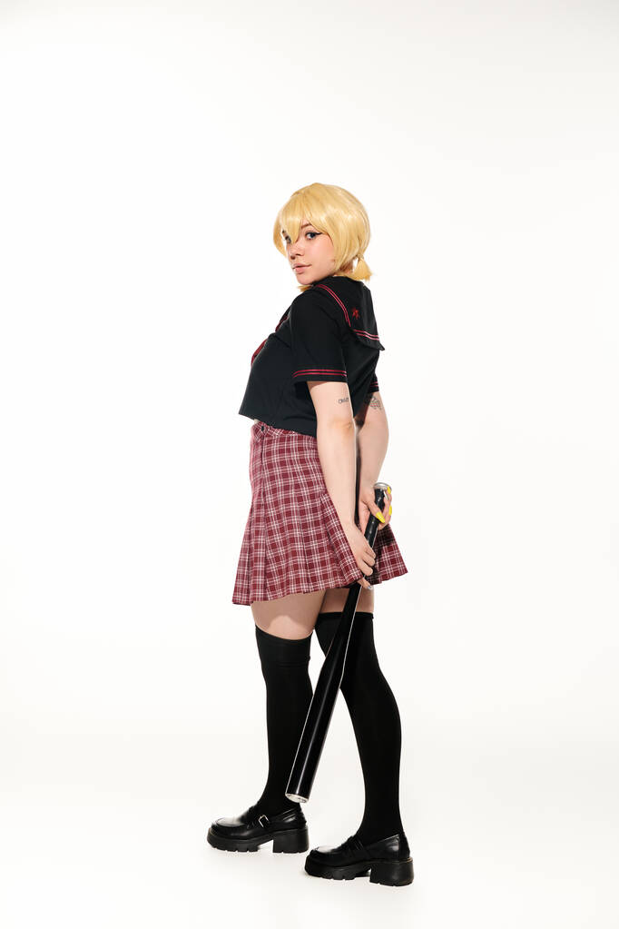 atrakcyjna kobieta w żółtej blond peruce i szkolnym mundurze z kijem baseballowym na białym, anime trend - Zdjęcie, obraz