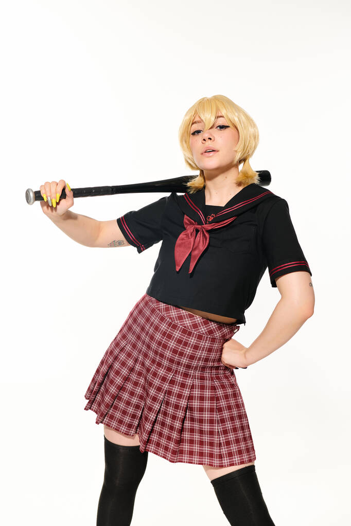 personaggio cosplay, donna altezzosa in uniforme scolastica con mazza da baseball e mano sull'anca su bianco - Foto, immagini