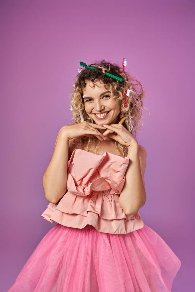 lächelnde Frau im rosafarbenen Outfit mit zum Gesicht erhobenen Händen, die vor rosa Hintergrund posiert, Konzept der Zahnfee - Foto, Bild