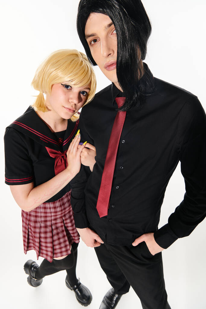 wide angle view of cosplay style couple in wigs and dark students uniform looking at camera on white - Photo, Image