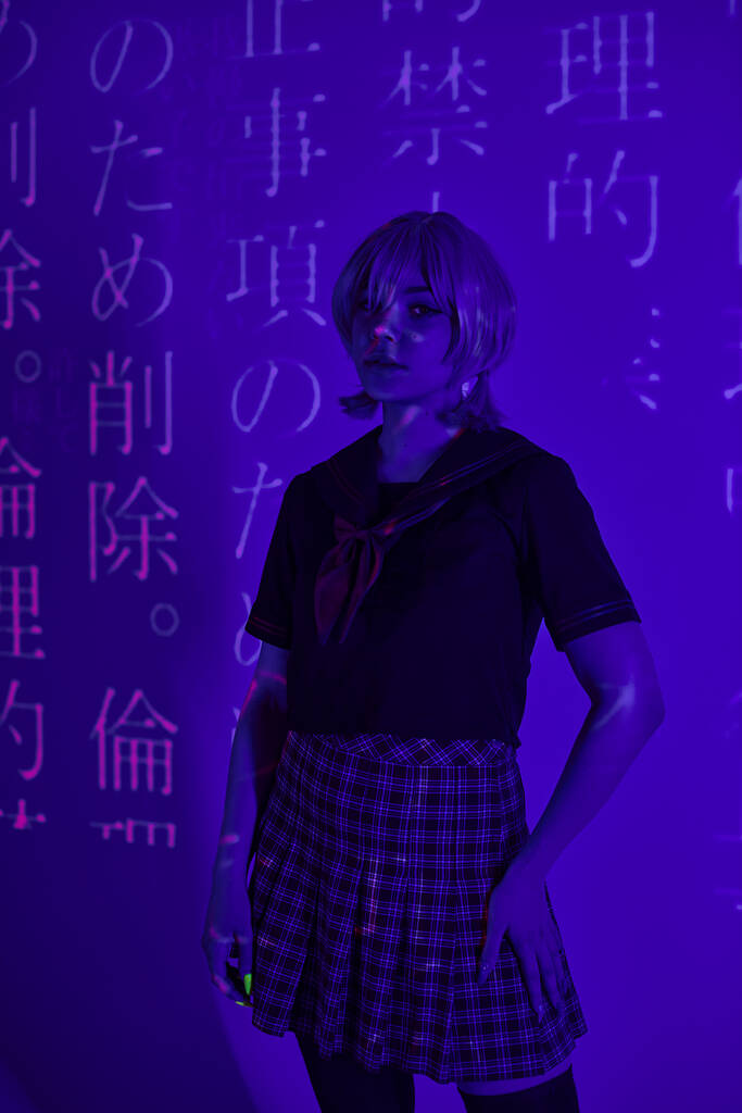 mulher cosplay em uniforme escolar de pé em luz de néon azul no fundo com projeção de hieróglifos - Foto, Imagem