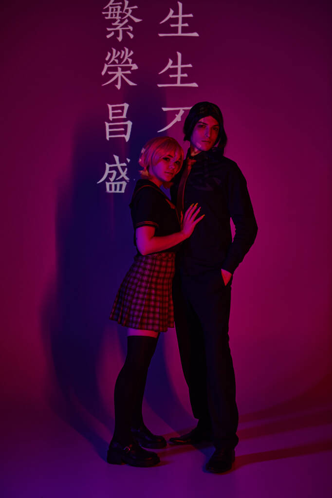 Пара студентов в форме в неоновом свете на фиолетовом фоне с иероглифами, модные косплееры - Фото, изображение