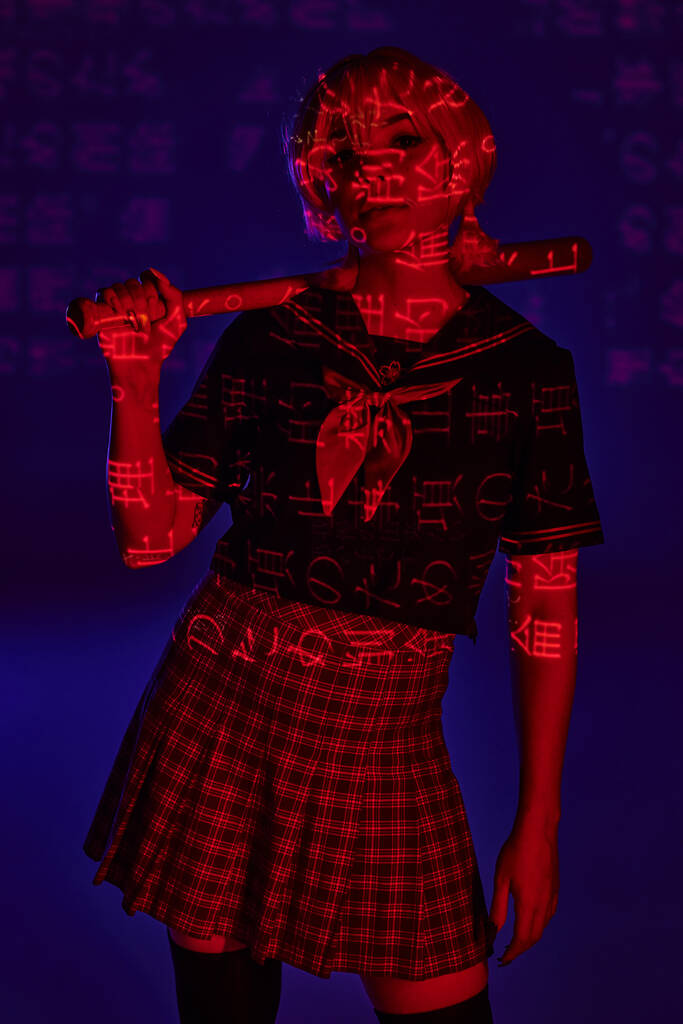 junge Anime-Frau in Schuluniform mit Baseballschläger in rotem Neonlicht mit Hieroglyphen auf blauem Hintergrund - Foto, Bild