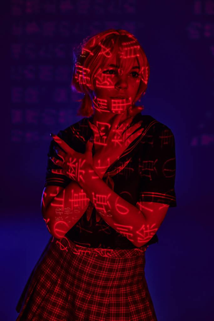 anime stílusú nő keresztbe tett karokkal néz félre neon kivetítése hieroglifák kék háttér - Fotó, kép