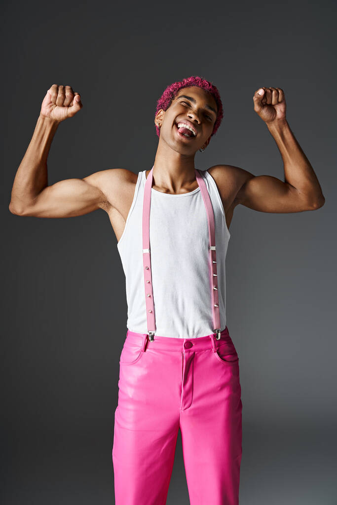 παιχνιδιάρης κομψός άντρας με ροζ μαλλιά που δείχνει μυς και προεξέχει γλώσσα, μόδα και στυλ - Φωτογραφία, εικόνα