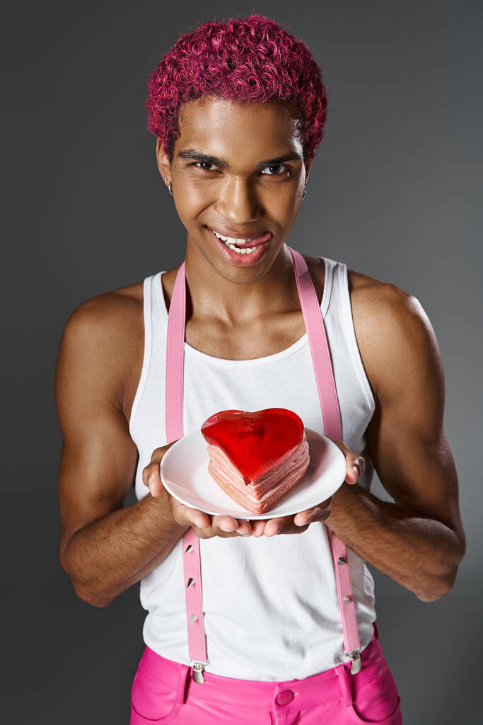 homme joyeux avec des cheveux roses montrant mini gâteau en forme de coeur et sortant la langue, la mode et le style - Photo, image