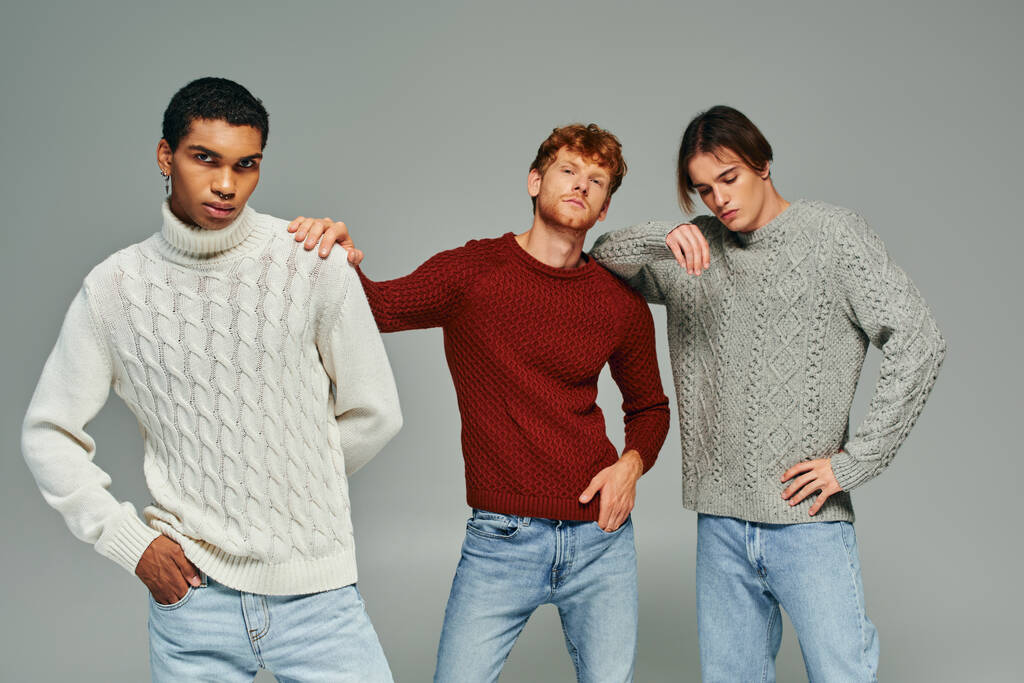 стильні міжрасові чоловічі моделі в яскравих повсякденних светрах, позують на сірому тлі, чоловіча сила - Фото, зображення