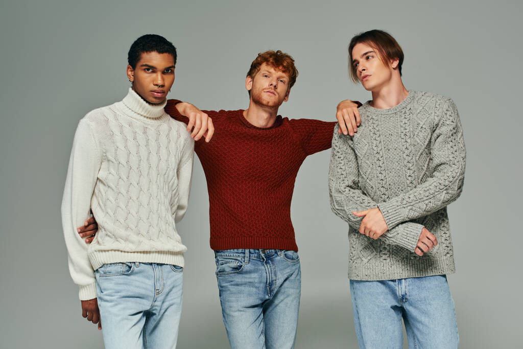três belos amigos do sexo masculino em suéteres vibrantes e jeans posando em fundo cinza, moda - Foto, Imagem