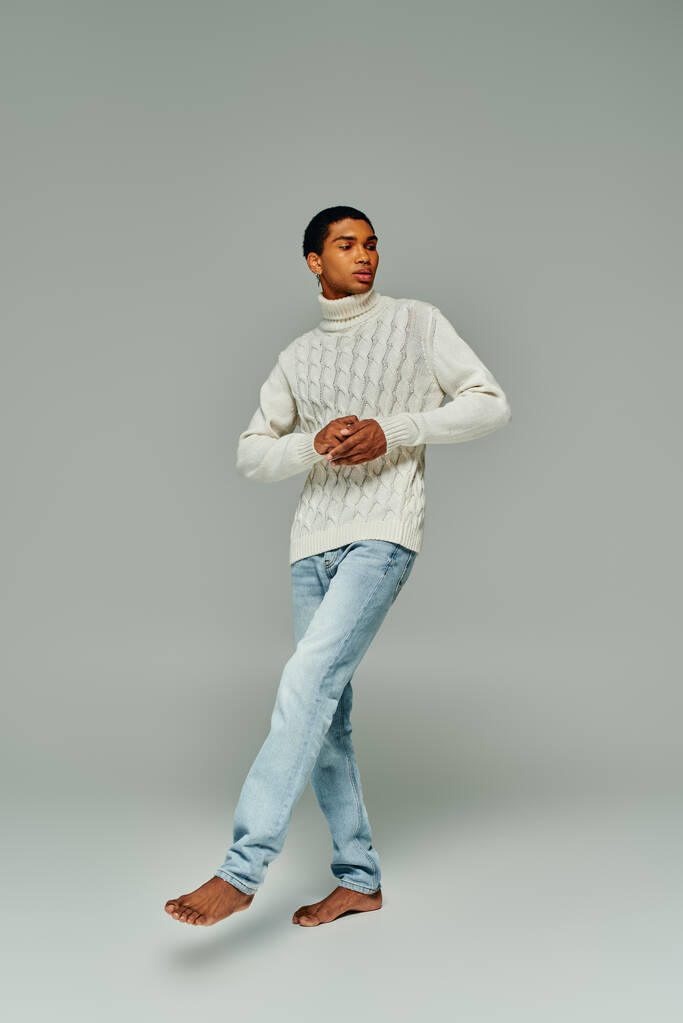 pohledný stylový africký americký muž v teplém svetru a džínách odvrací pohled, módní koncept - Fotografie, Obrázek