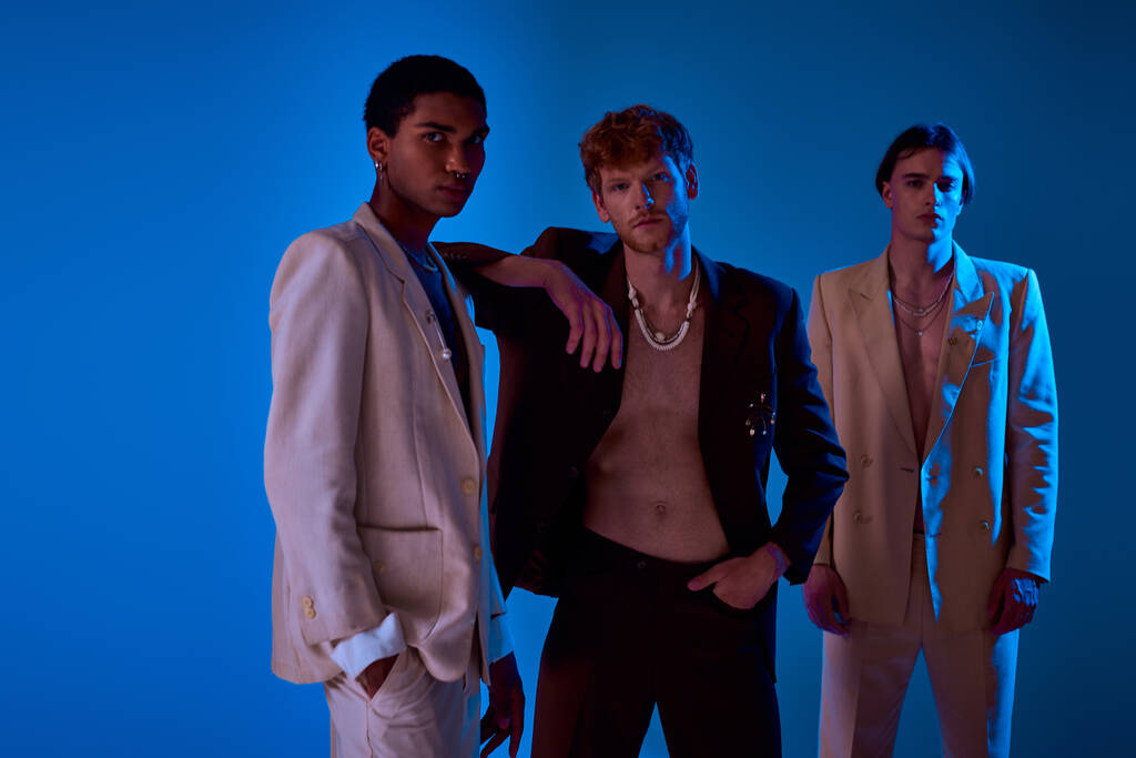 three multicultural male models in vivid suits posing in neon lights, looking at camera, men power - Photo, Image