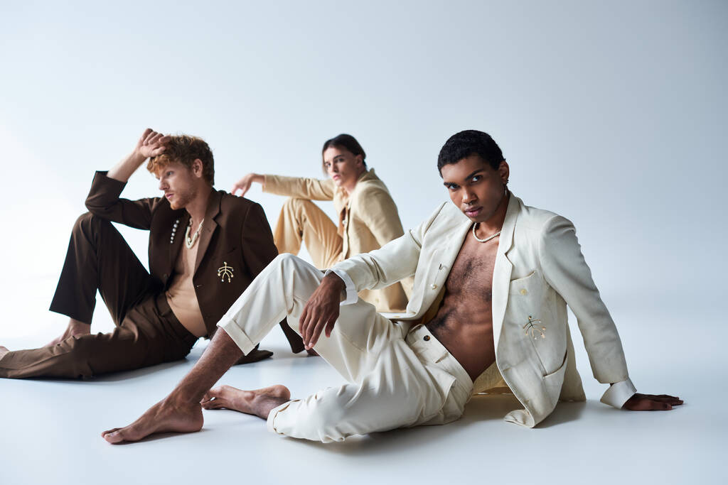 gutaussehende multikulturelle männliche Models in edlen Anzügen posieren auf dem Boden vor grauem Hintergrund, Männerpower - Foto, Bild