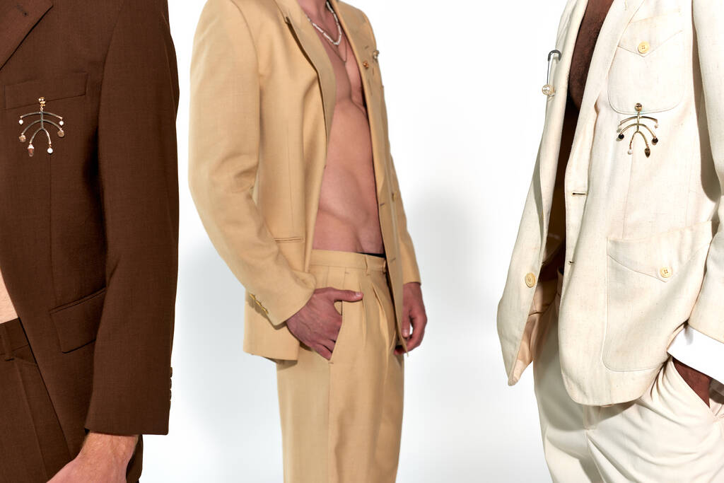 przycięty widok trzech młodych wielonarodowych mężczyzn w rozpiętych eleganckich garniturach na szarym tle, moda - Zdjęcie, obraz