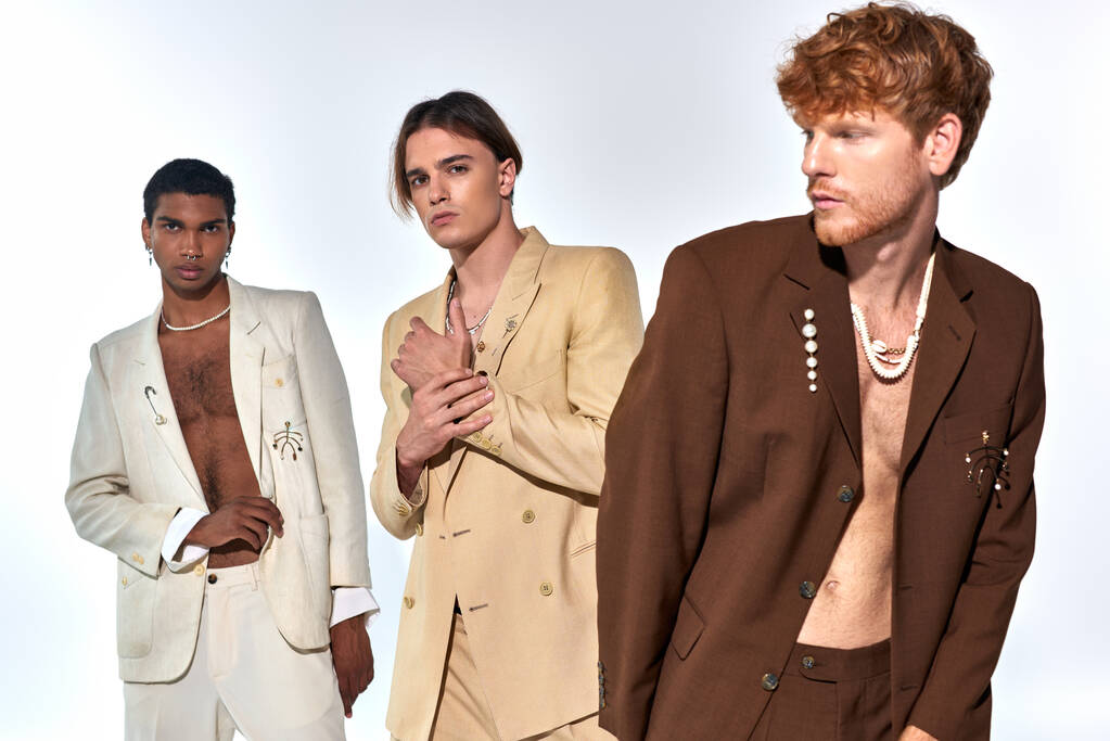 drie jonge diverse mannen in elegante stijlvolle pakken met accessoires poseren op witte achtergrond - Foto, afbeelding