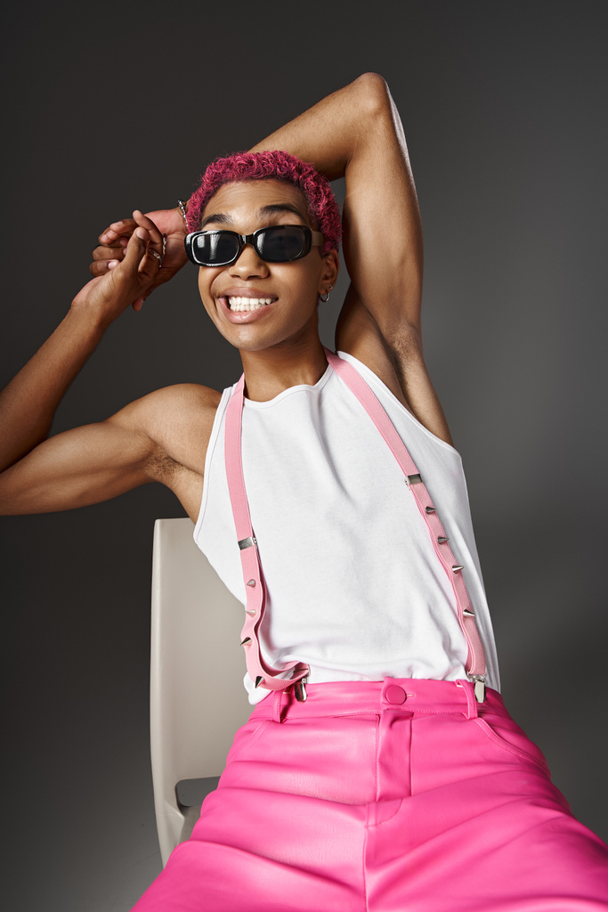 giocoso giovanotto con capelli rosa e bretelle sorridenti indossando occhiali da sole, concetto di moda - Foto, immagini