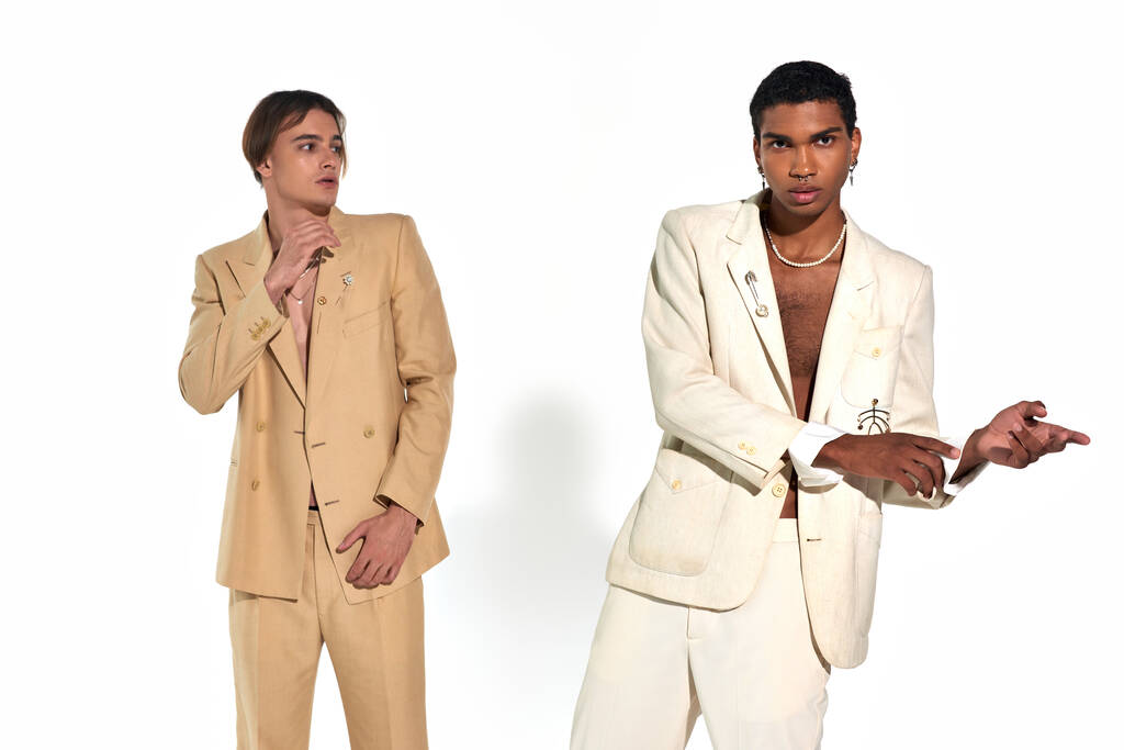 dúo multicultural con estilo en trajes elegantes con accesorios posando en movimiento sobre fondo blanco - Foto, Imagen